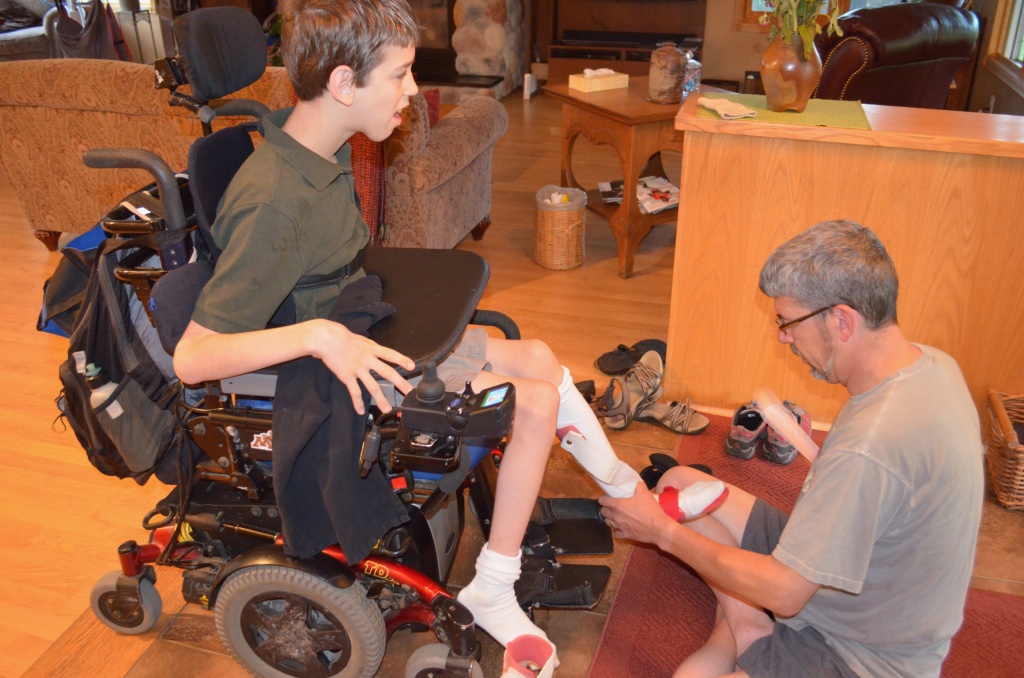 Justin in wheelchair, dad holding Justin's foot
