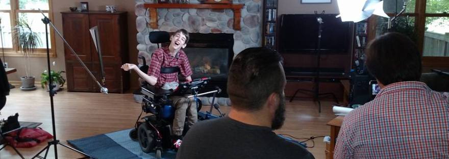 Justin in wheelchair with movie lights, 2 men looking at him with video camera