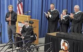 Justin in graduation gown near podium 4 adults standing and applauding