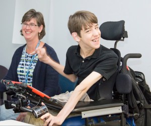 Justin sitting in wheelchair with communication device, mom sitting next to him