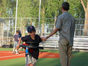Justin in gait trainer giving high five to his dad on accessible baseball field