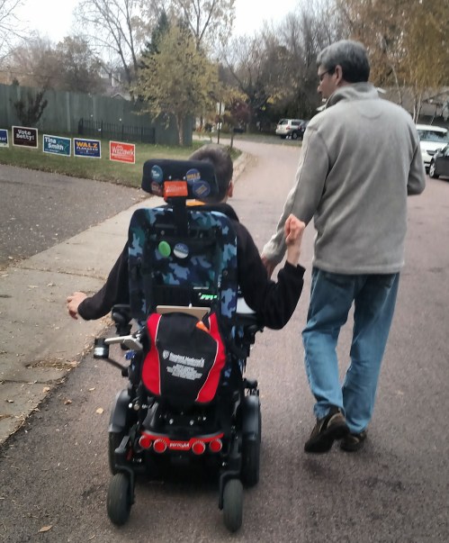 Back of man and Justin in his wheelchair walking down street