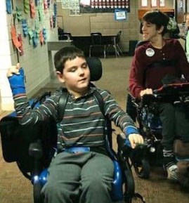 Boy and young man driving power wheelchairs in school hallway