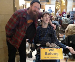 Man with arm around Justin, We belong in the community sign hanging on front of Justin's wheelchair