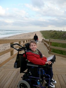 Justin as a boy at top of board walk ramp with sandy beach and ocean