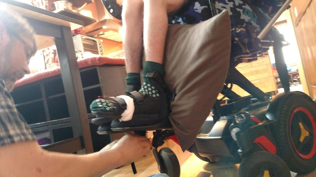 Dad working on wheelchair footrests with Justin's feet strapped in