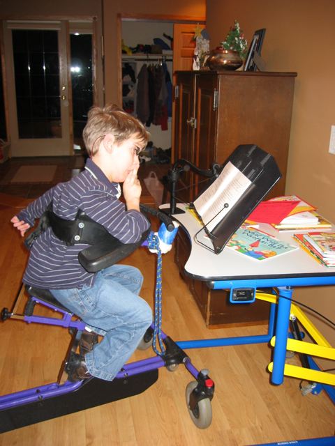 Justin, around 8 years old in gait trainer looking at book on book holder