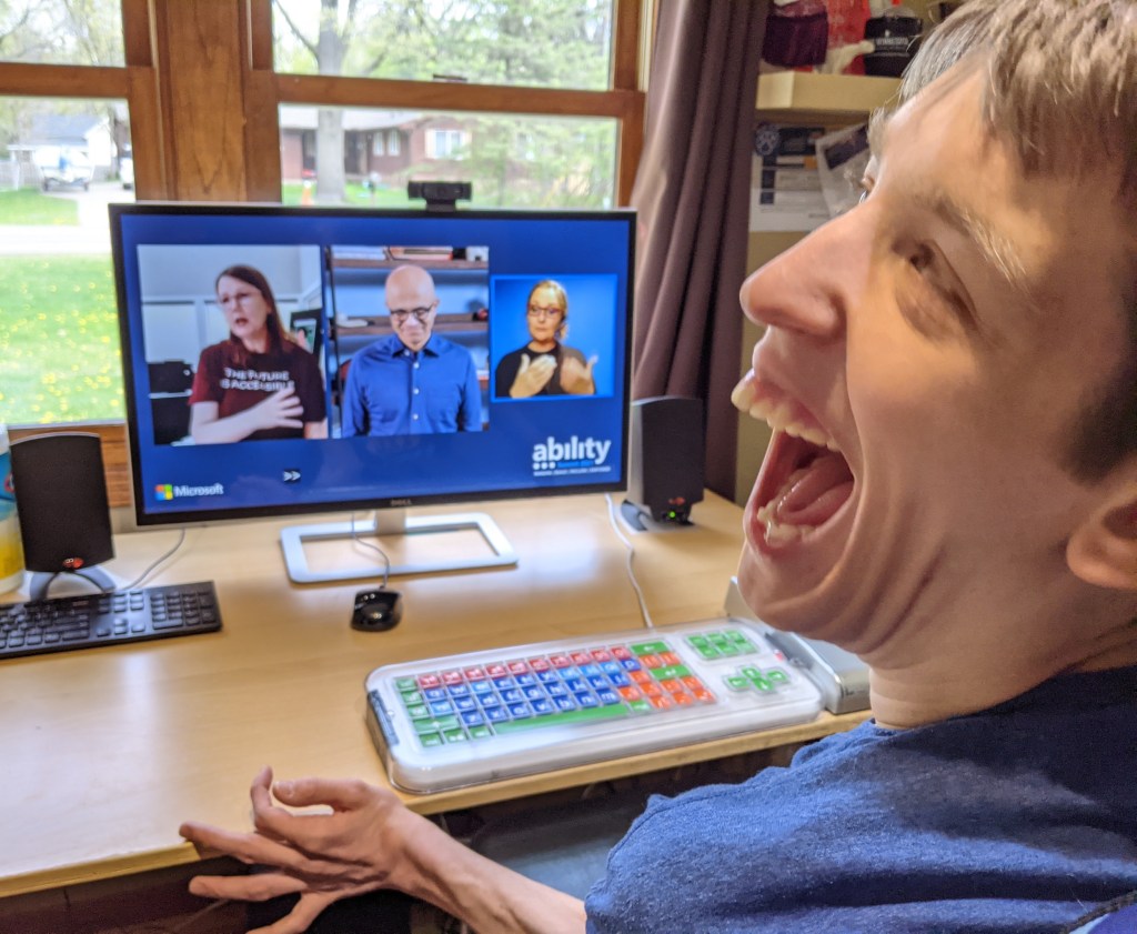 Justin smiling, watching Jenny Lay-Flurry and Satya Nadella and ASL interpreter on computer monitor