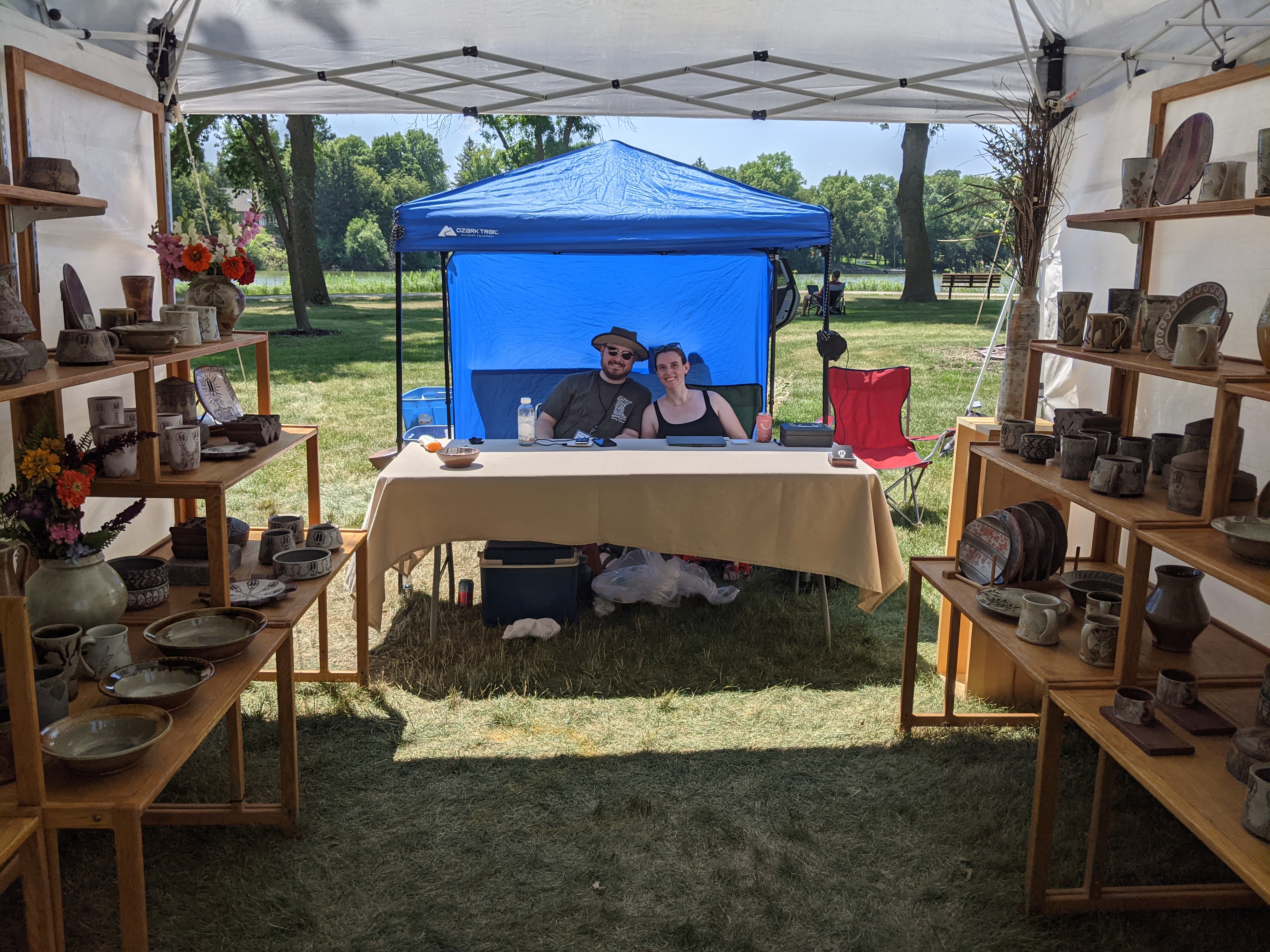 Man and woman sitting behind table, pottery on shelves
