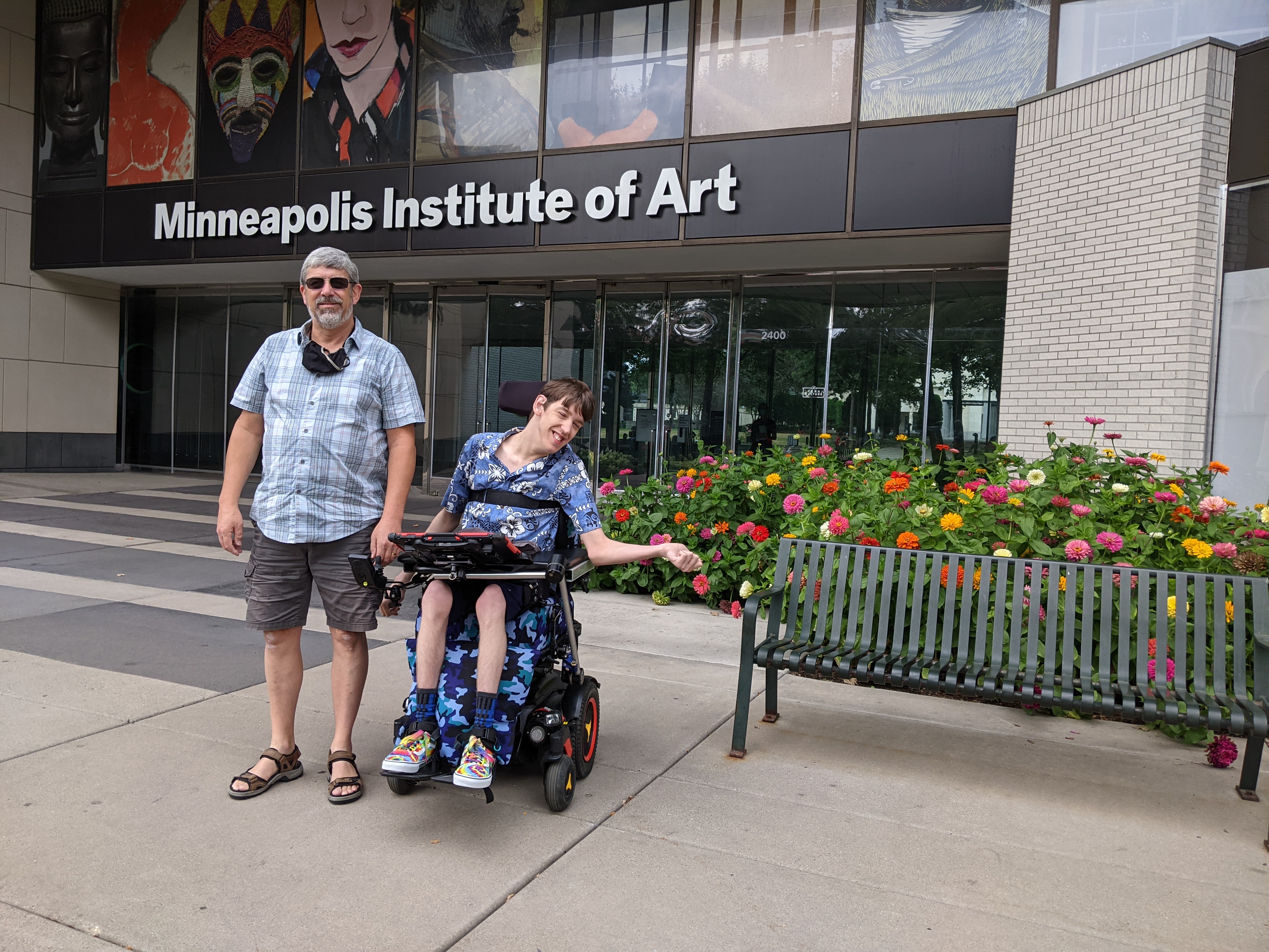 Justin in wheelchair, his dad, in front of Minneapolis Institute of Arts entrance, dahlias blooming