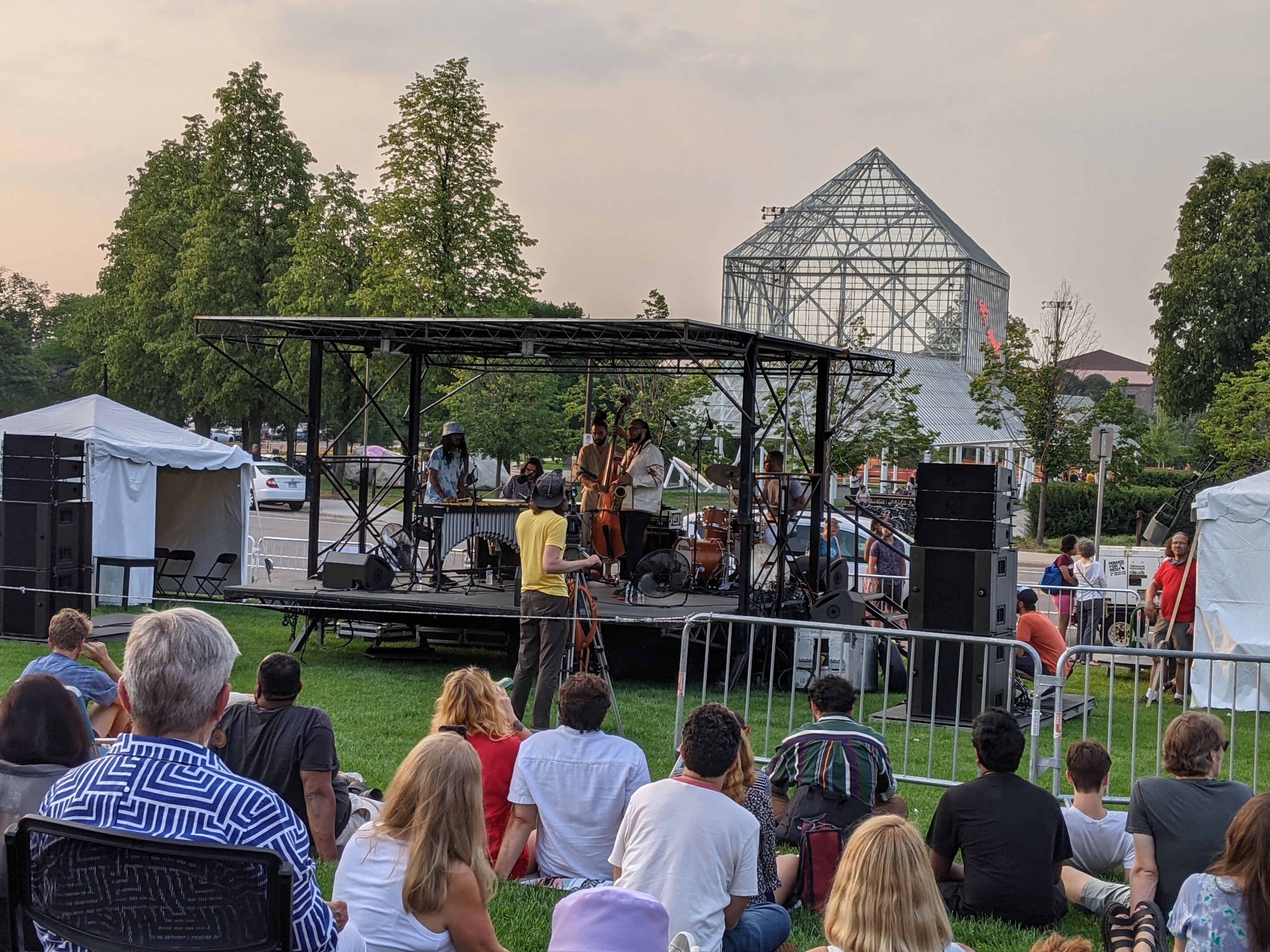 Band on stage, people sitting on grassy lawn, Walker Sculpture Garden behind