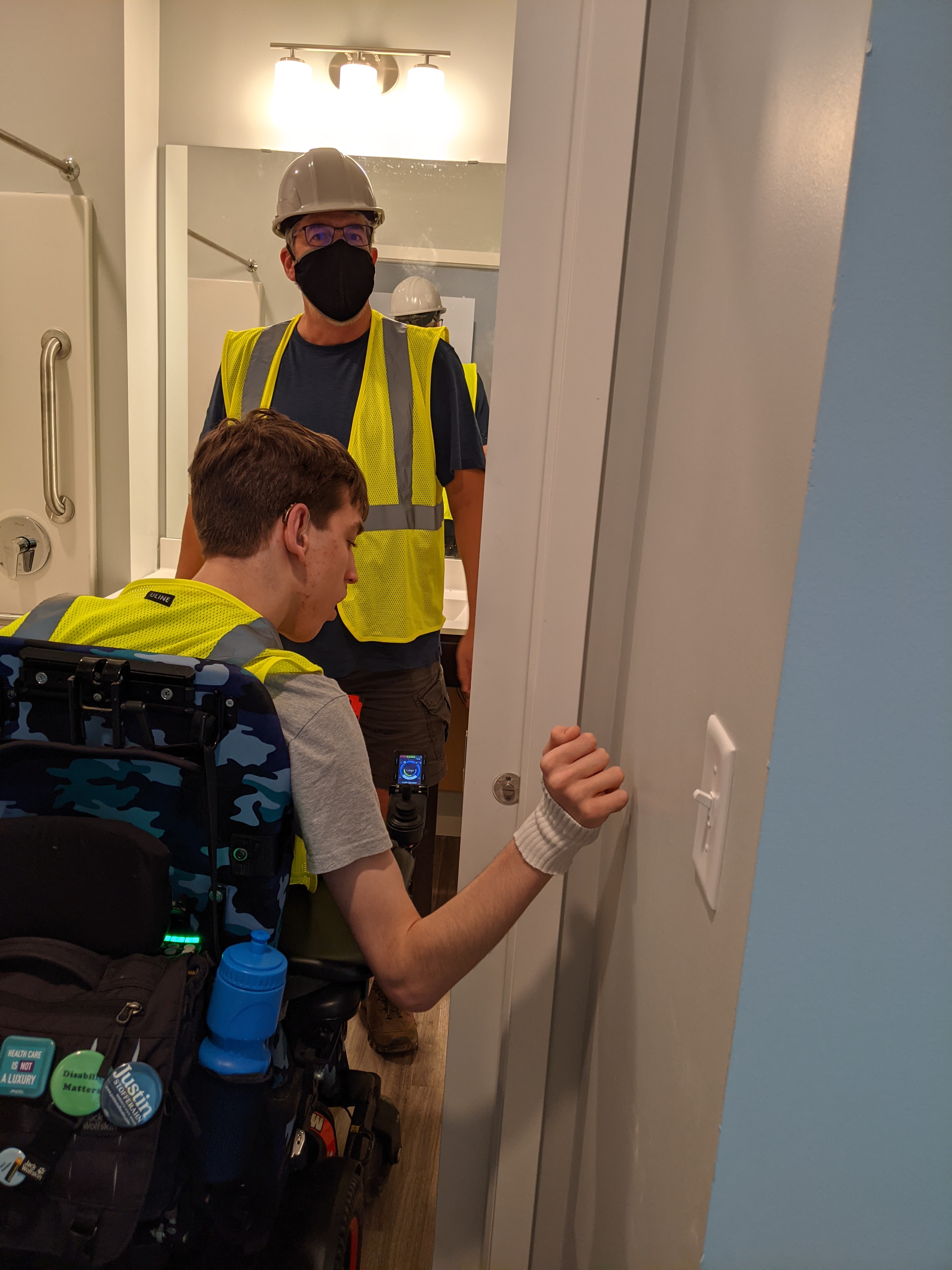 Justin in power chair and his dad entering bathroom, pocket door sticking out 4 inches