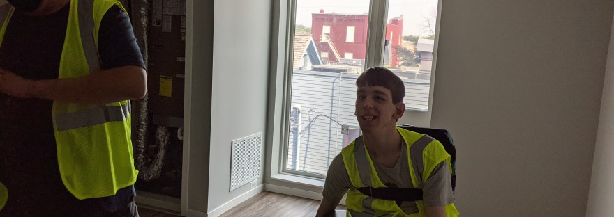Justin smiling, Dad with vest and helmet, empty living room