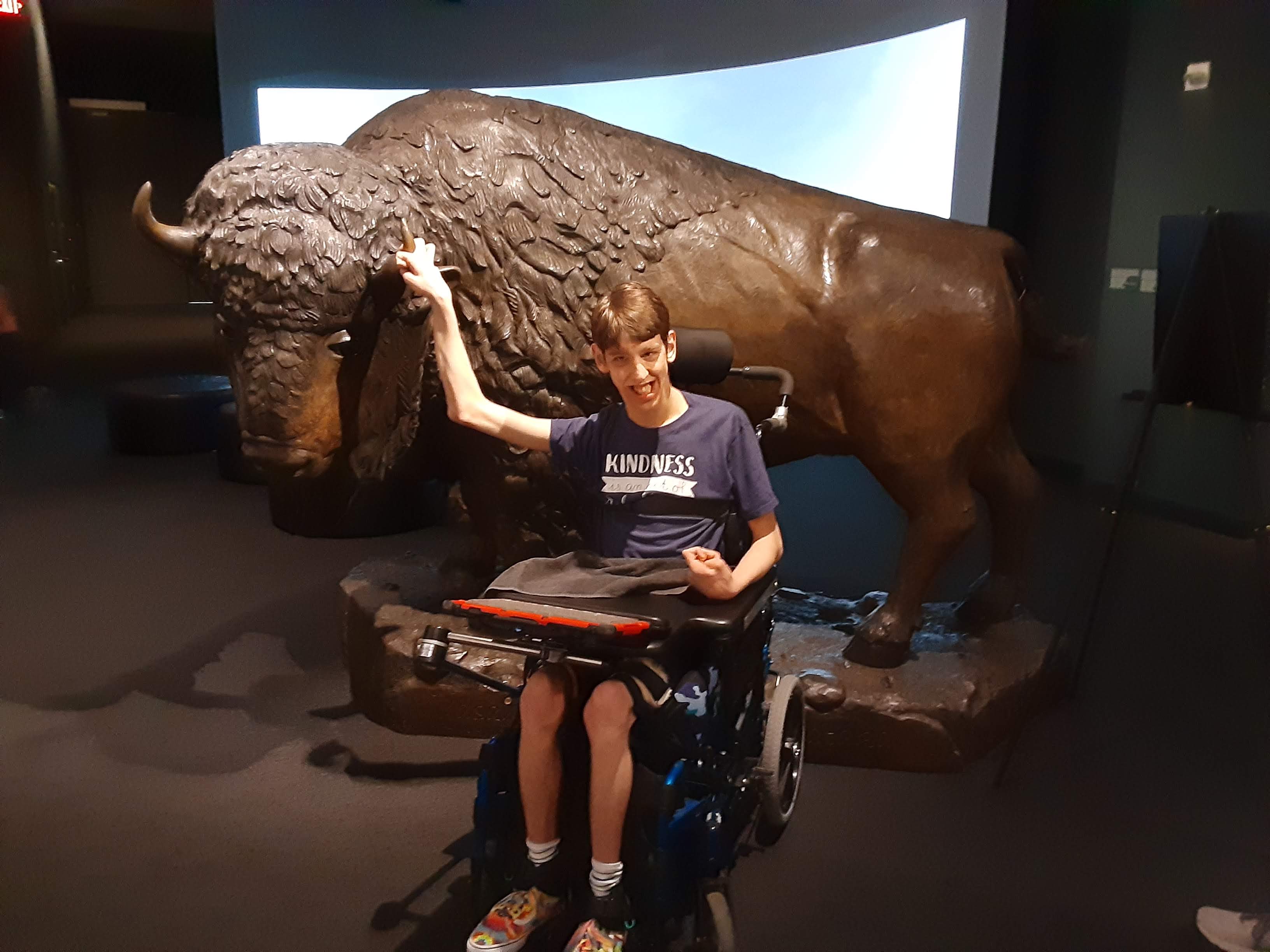 Justin in wheelchair, holding horn of bison sculpture in museum