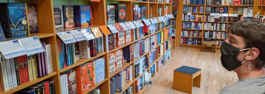 Justin wearing mask, sitting in wheelchair, looking at bookshelves in bookstore