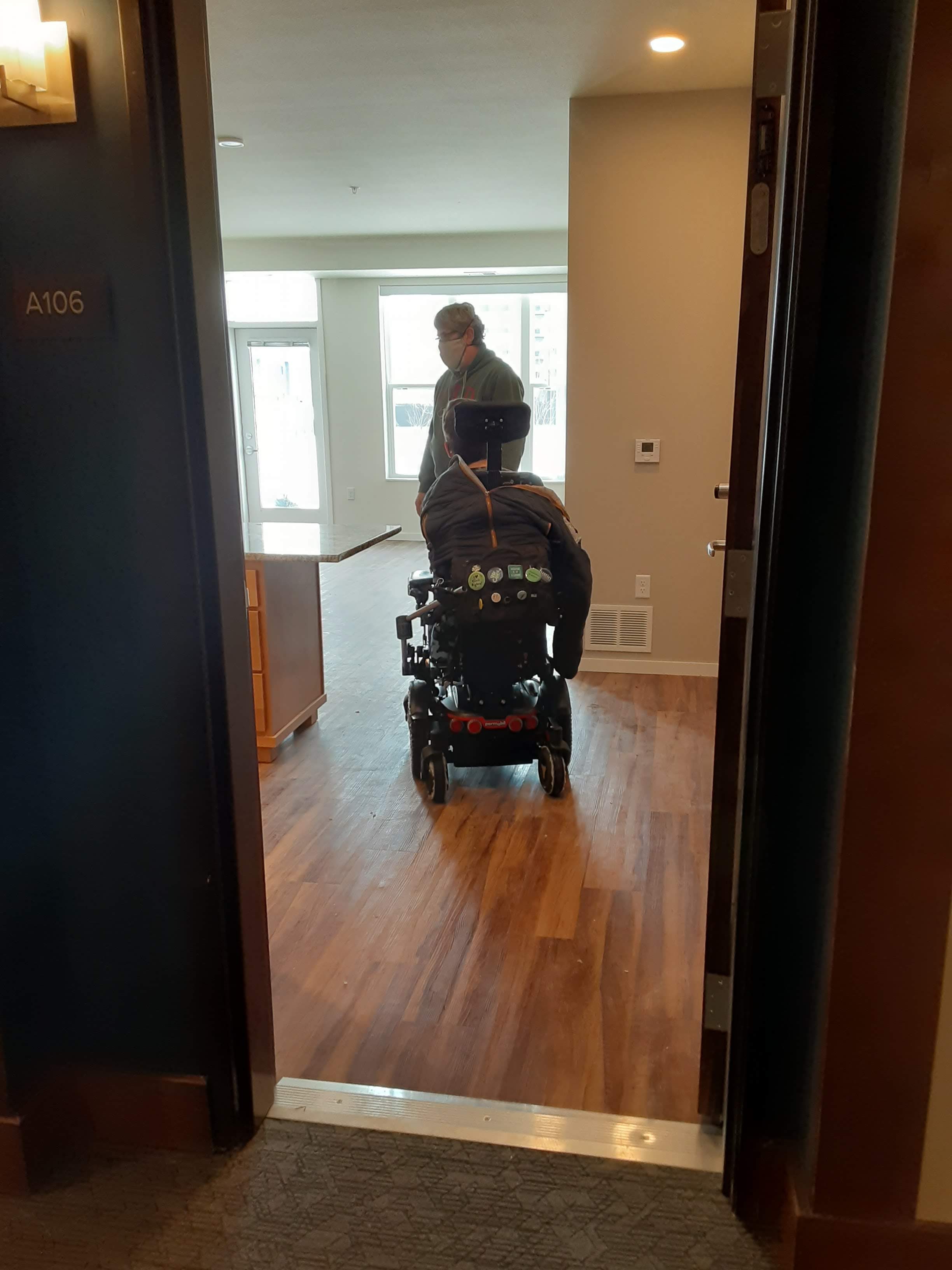 the back of Justin in his power wheelchair next to his dad in empty apartment