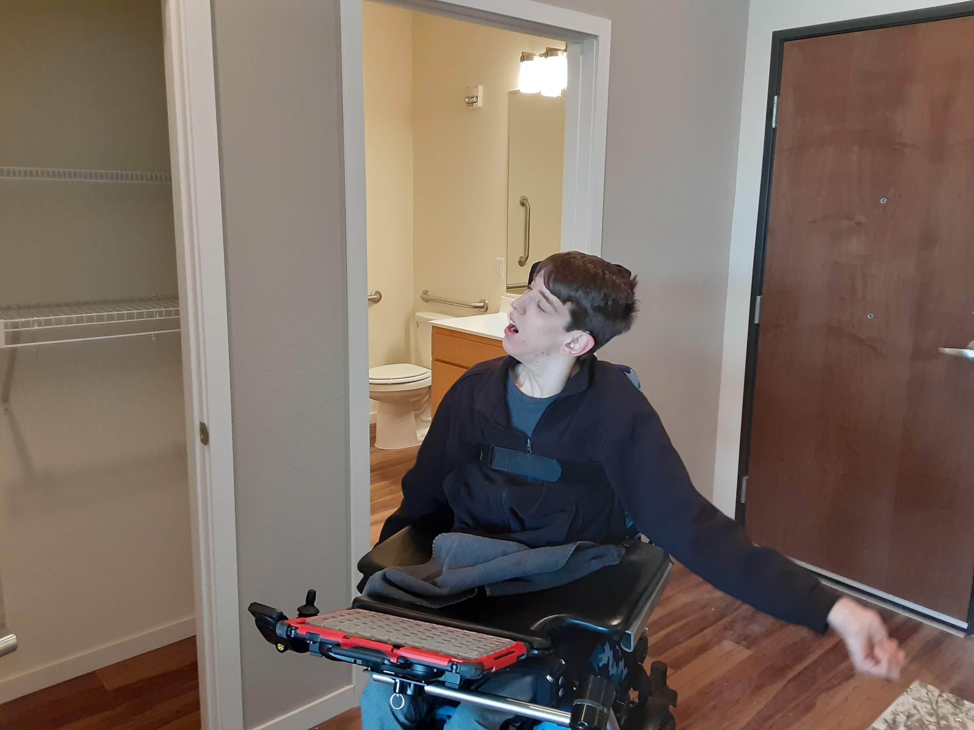 Justin in wheelchair in apartment entry, bathroom in back
