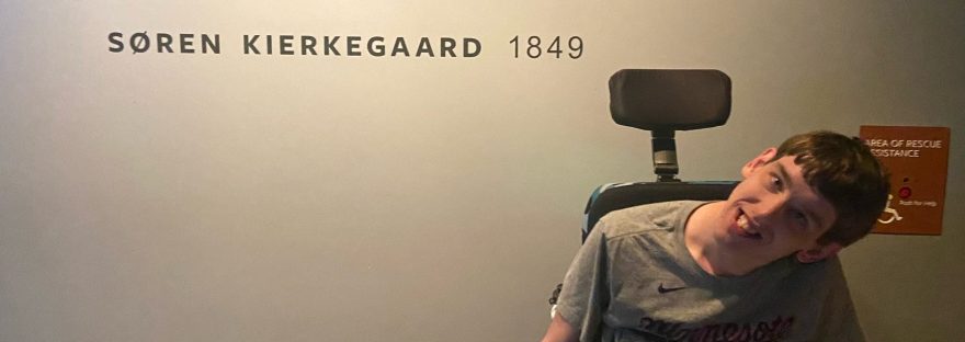 Young man in wheelchair in front of quote painted on wall by Soren Kierkegaard, 1849, "Once you label me you negate me."
