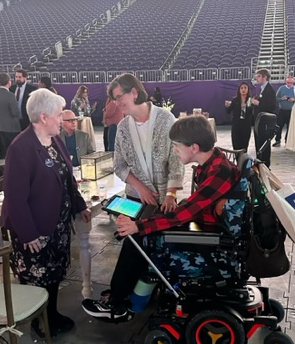 Justin in power wheelchair next to his mom in conversation with Ramsey County Commissioner Victoria Reinhardt, in US Bank Stadium