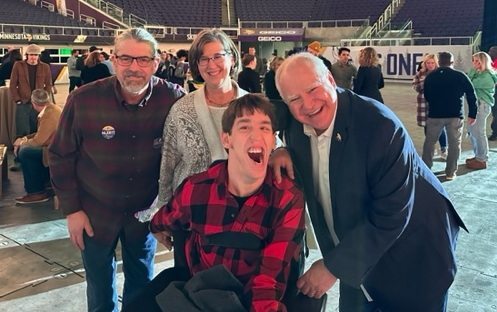 Justin in wheelchair next to Governor Walz, Justin's mom and dad standing behind, all smiling, people behind them