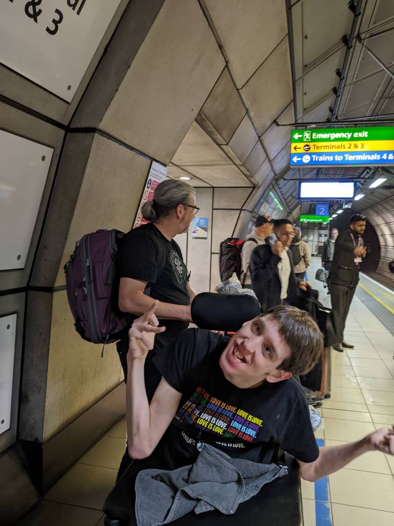 Justin seated in wheelchair, people standing behind, underground tube station