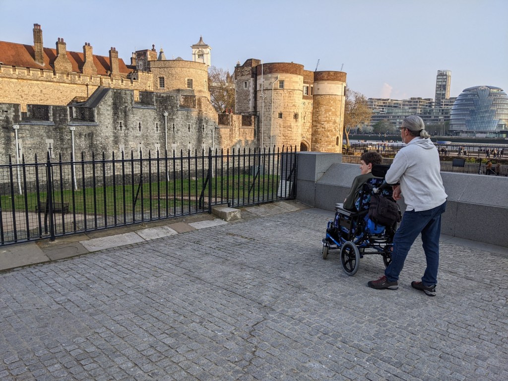 Justin in manual wheelchair with his dad looking at Tower of London