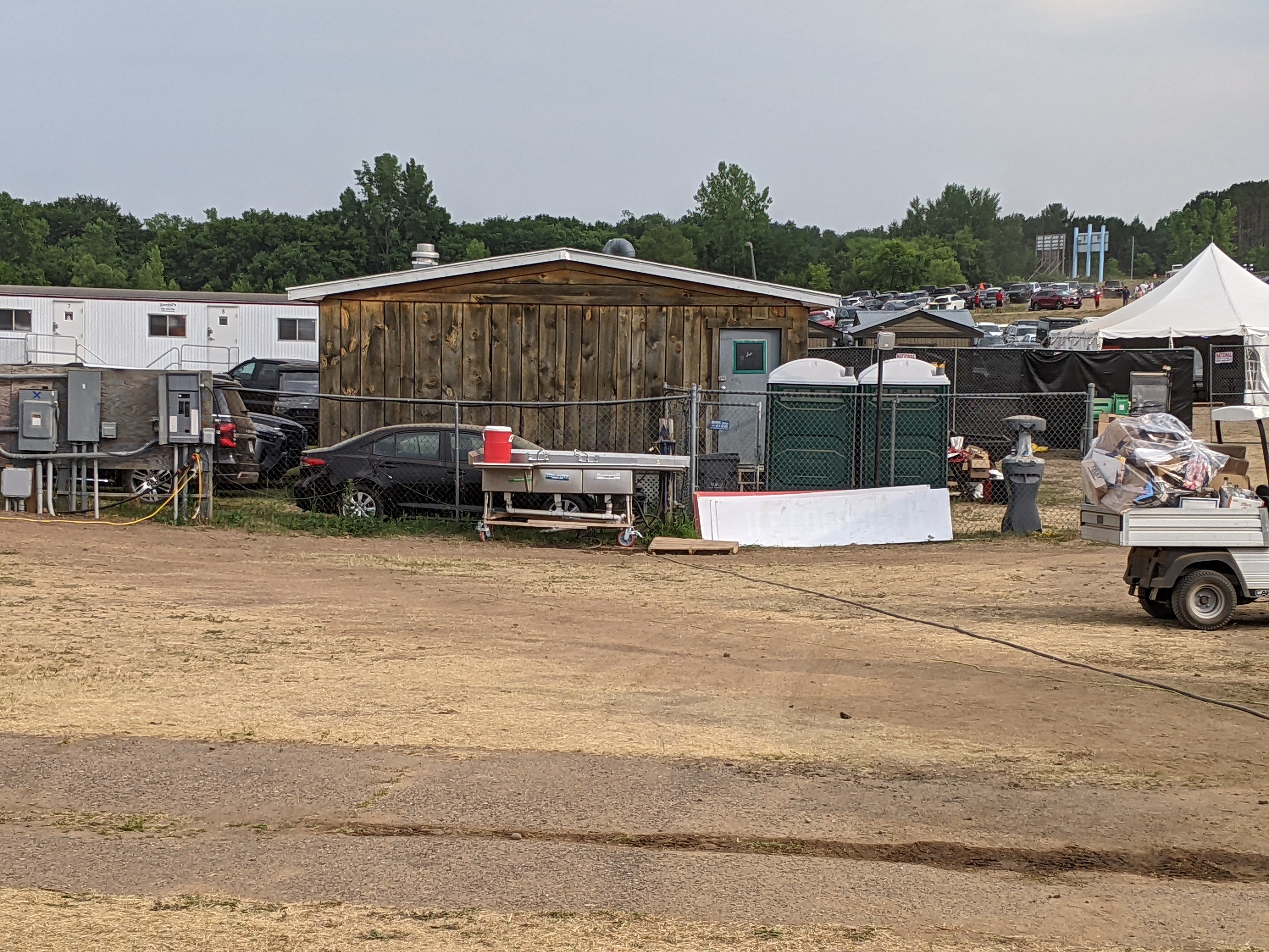 portable temporary sink near fence, porta-potties, car, tent, trailers, dirt and dried grass