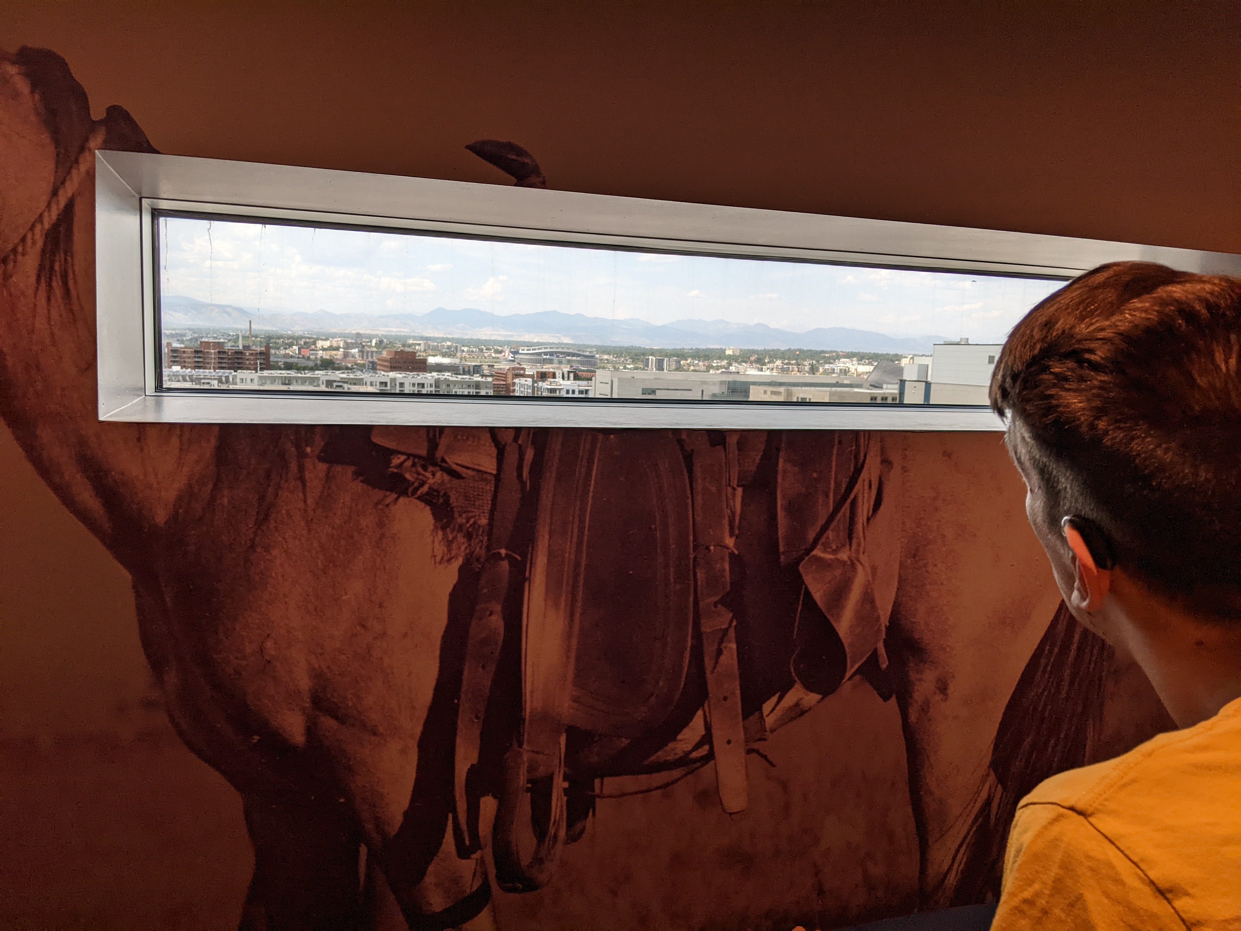 back of Justin looking out museum window looking at Denver skyline and foothills
