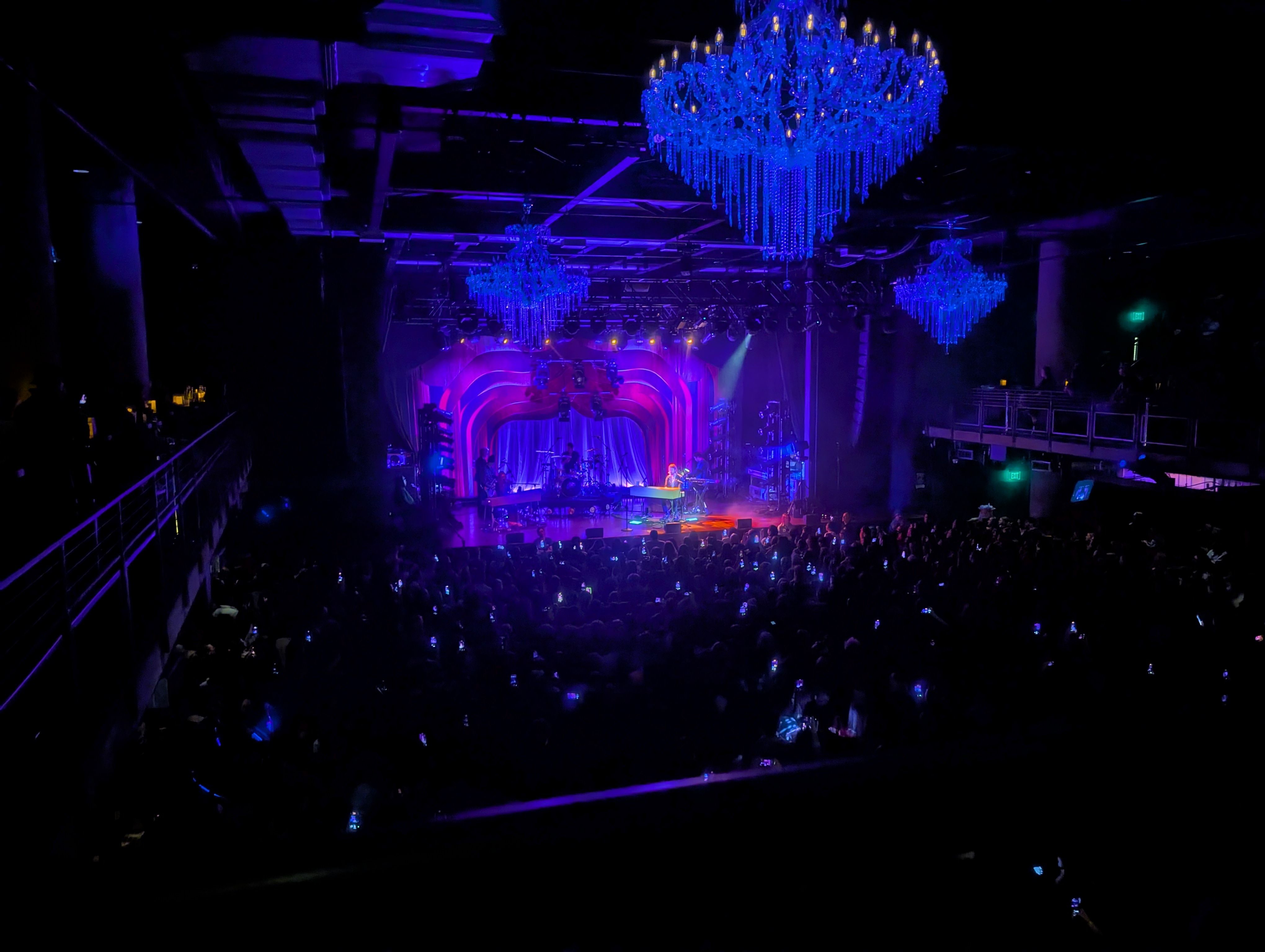 Finneas and band on stage, crowd on main floor, giant chandeliers, purple lighting