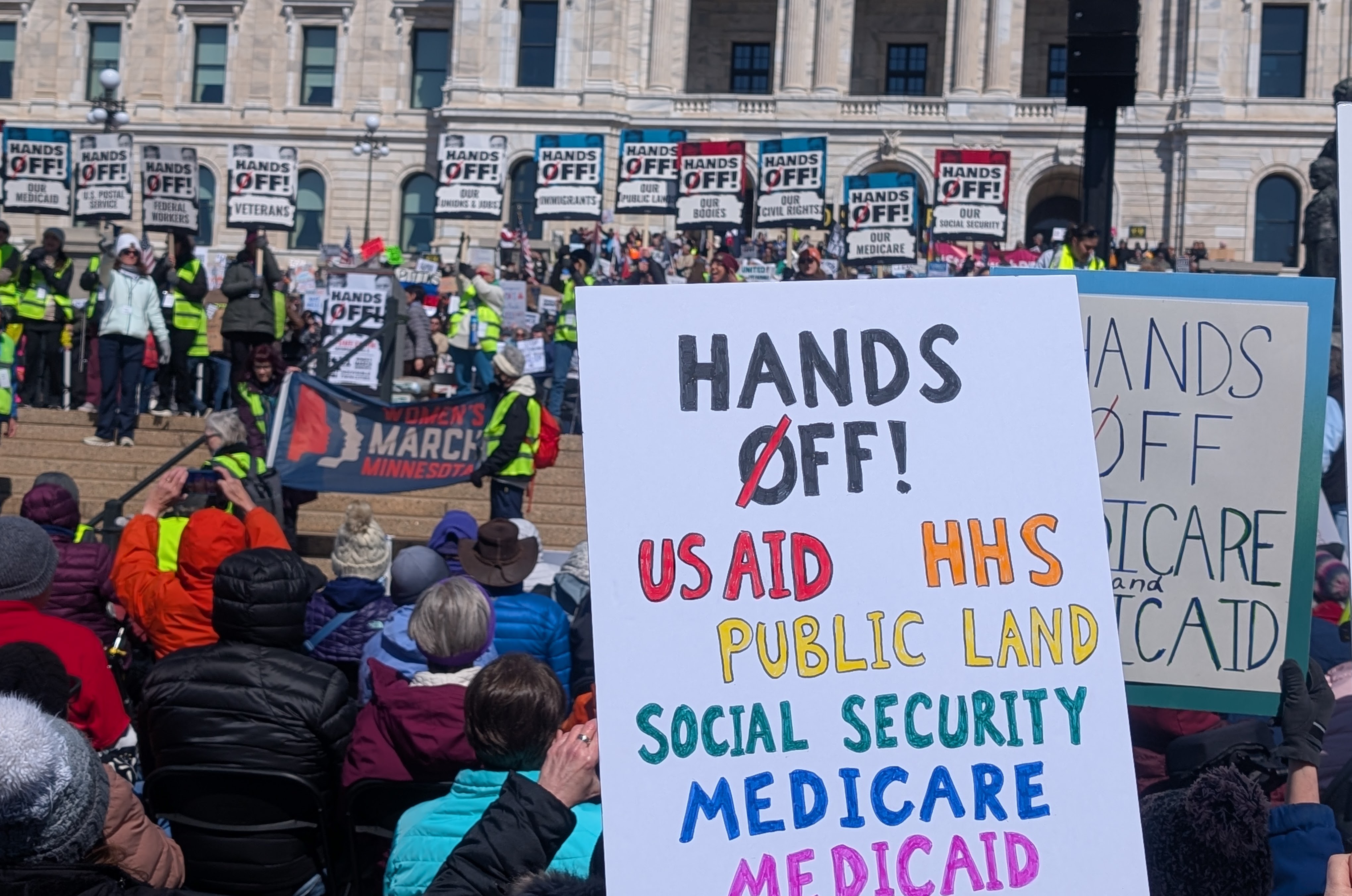 Sign in crowd that says Hands off US Aid, HHS, Public Land, Social Security, Medicare, Medicaid