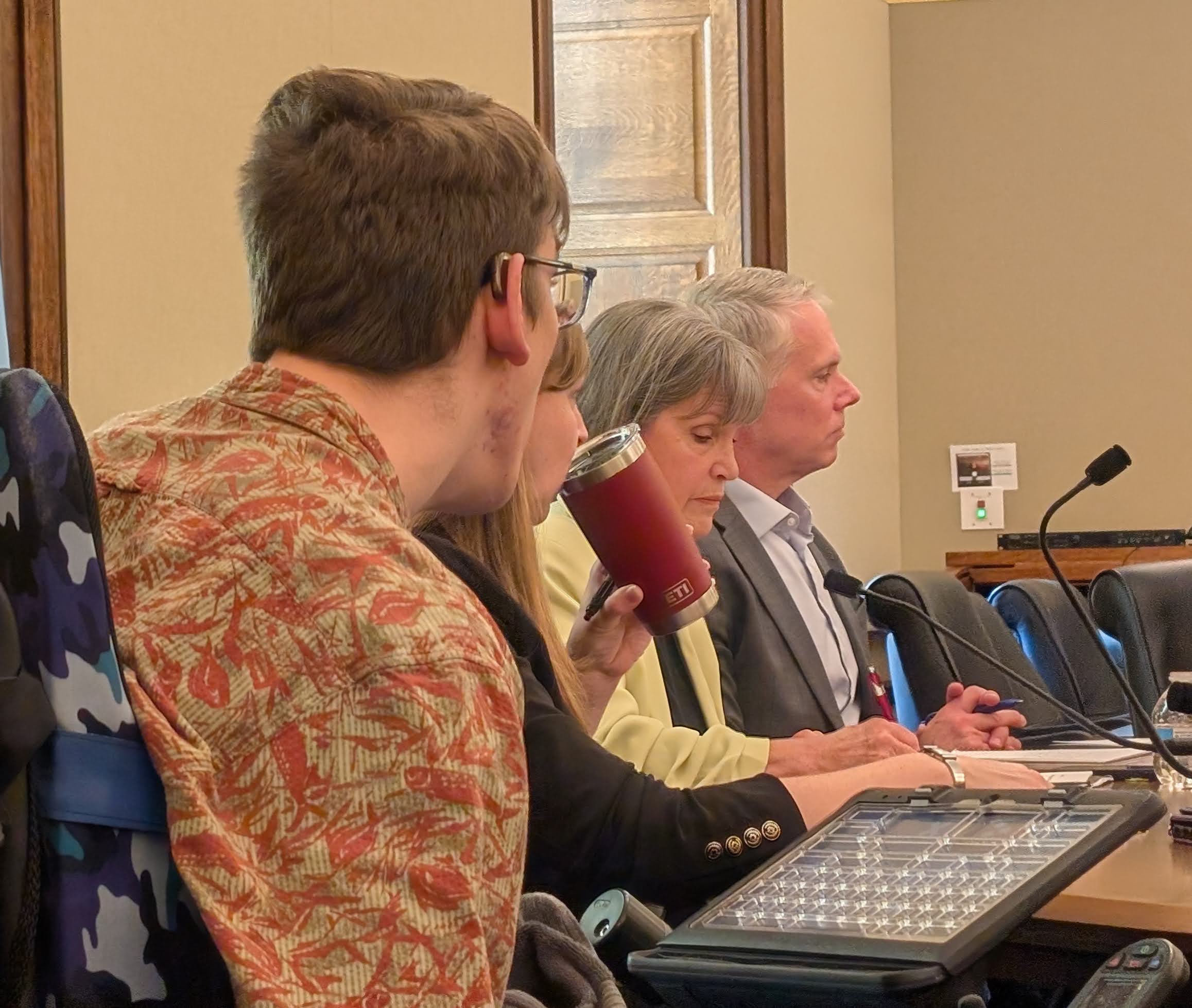 Justin, State Rep Amanda Hemmingsen-Jaeger holding a travel mug, Representative McCollum, and man seated next to her. All looking serious.
