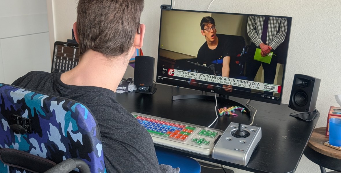 Justin sitting at his computer with accessible keyboard watching a kstp news story that's showing a picture of him in his wheelchair