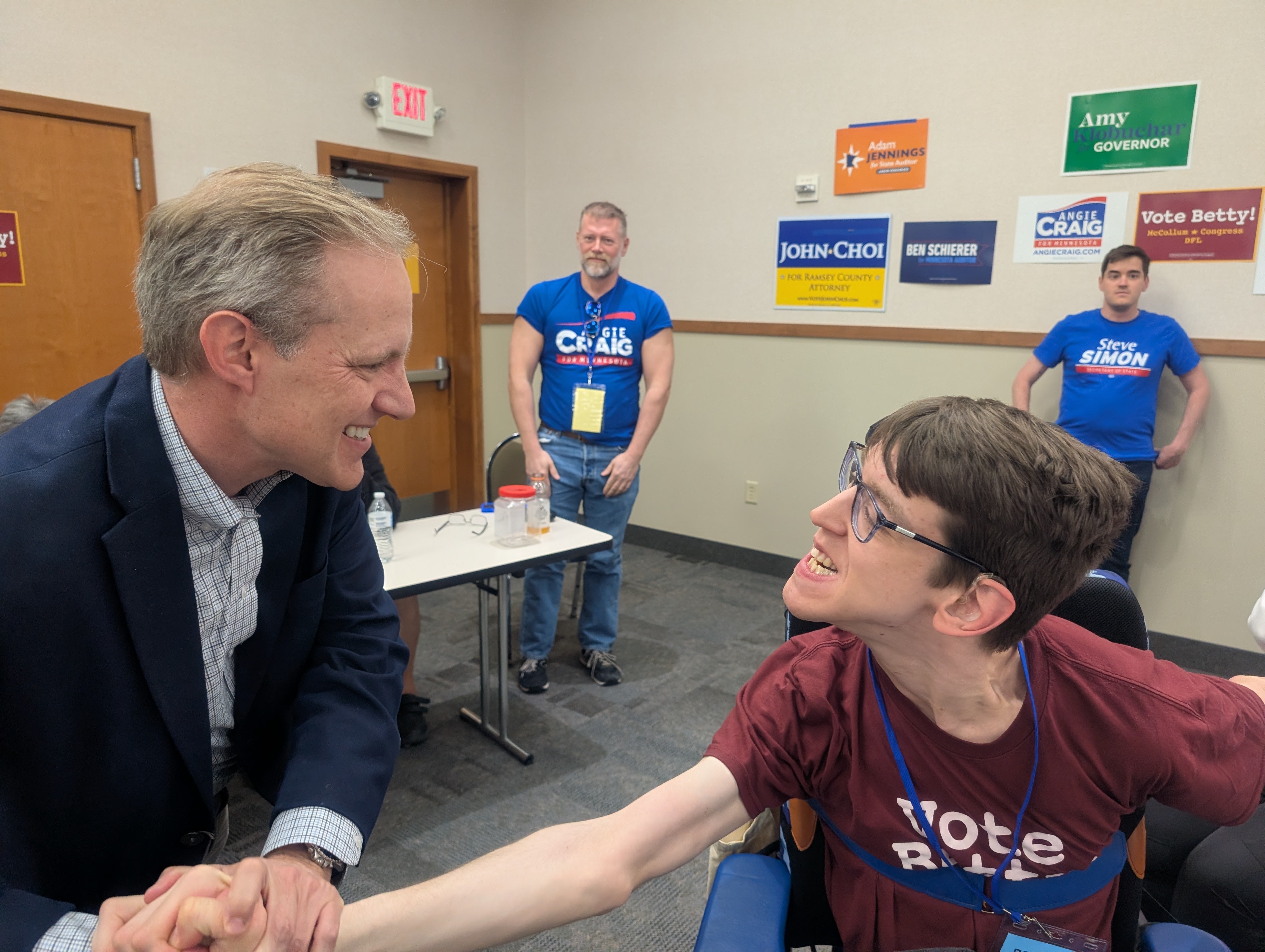 Secretary of State Steve Simon shaking hands with Justin, people in background 